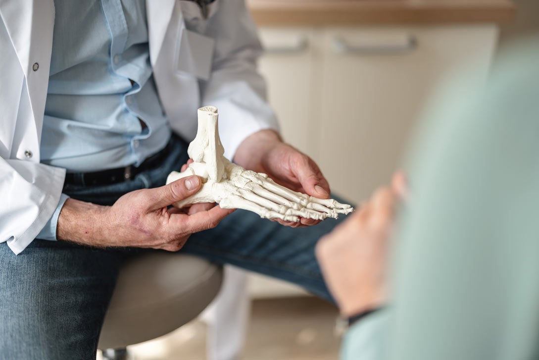 Doctor holding model of foot bones, explaining arthritis
