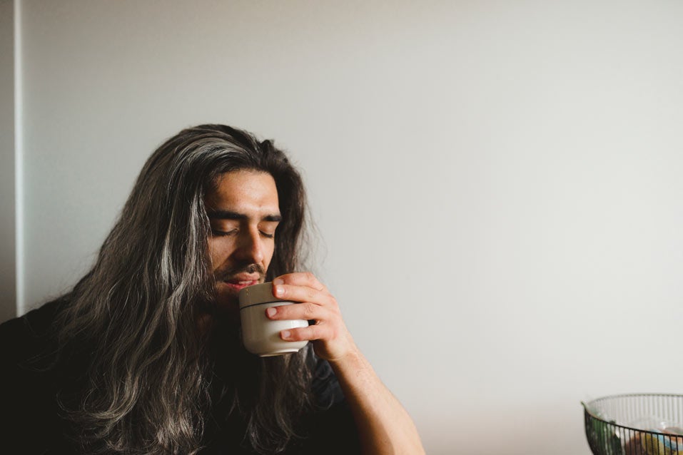 Man with long hair drinking herbal tea from a mug
