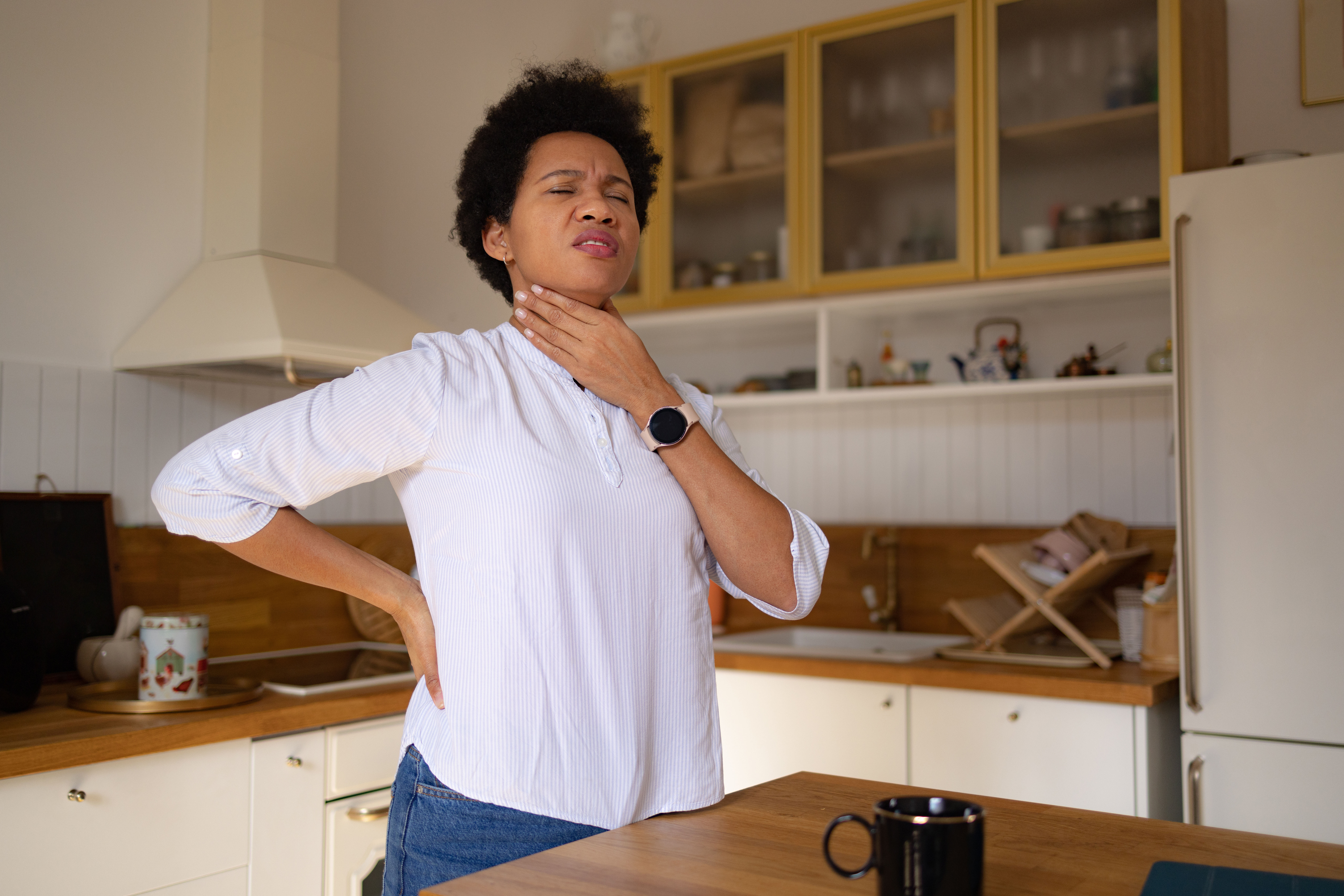 Woman in kitchen holding her throat in pain