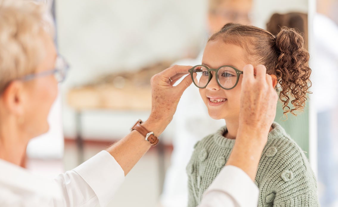 Young curly-haired girl getting glasses put on her face by a doctor