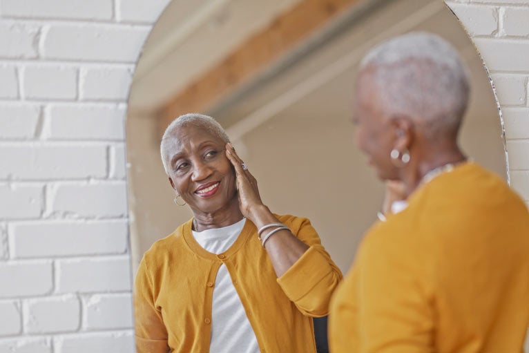 Older black woman looking in mirror and touching her face