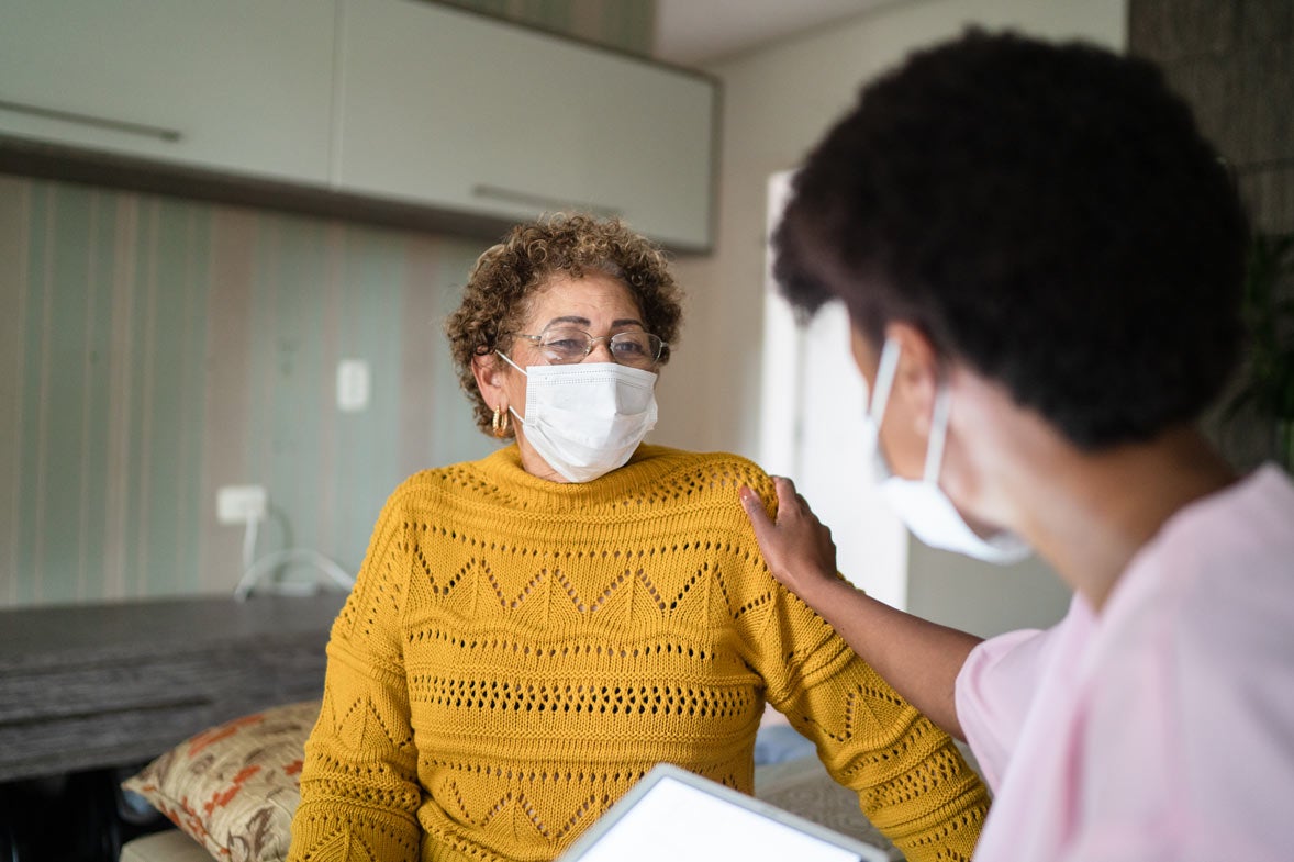 Older woman wearing mask and talking with doctor in exam room